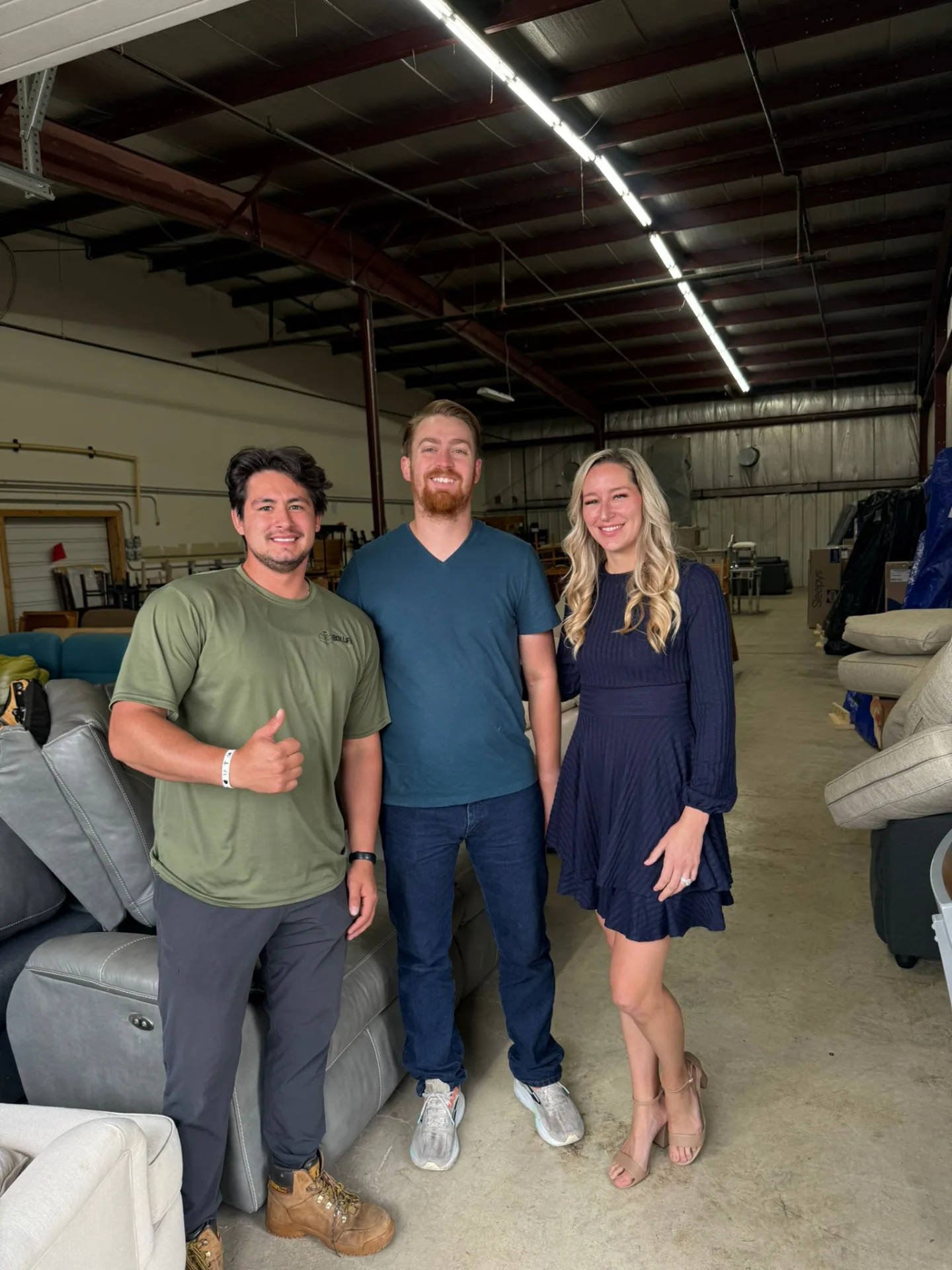 Box Life Moving crew members with a happy customer giving a thumbs up inside a warehouse full of furniture